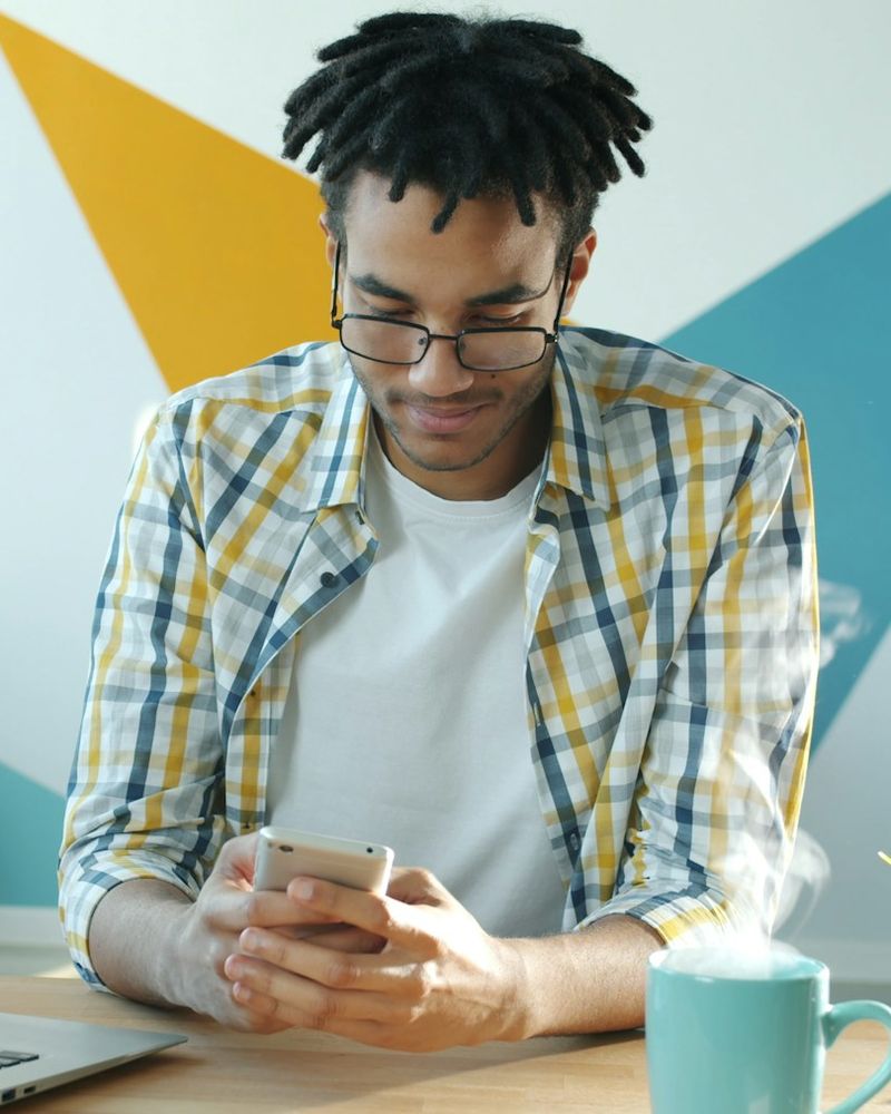 A man in glasses at his desk, reading something on his phone